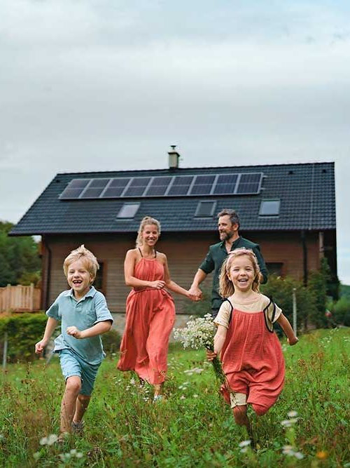 Glückliche Familie läuft mit Sonnenkollektoren in der Nähe ihres Hauses. Alternative Energie, Ressourcenschonung und nachhaltiges Lebensstilkonzept.